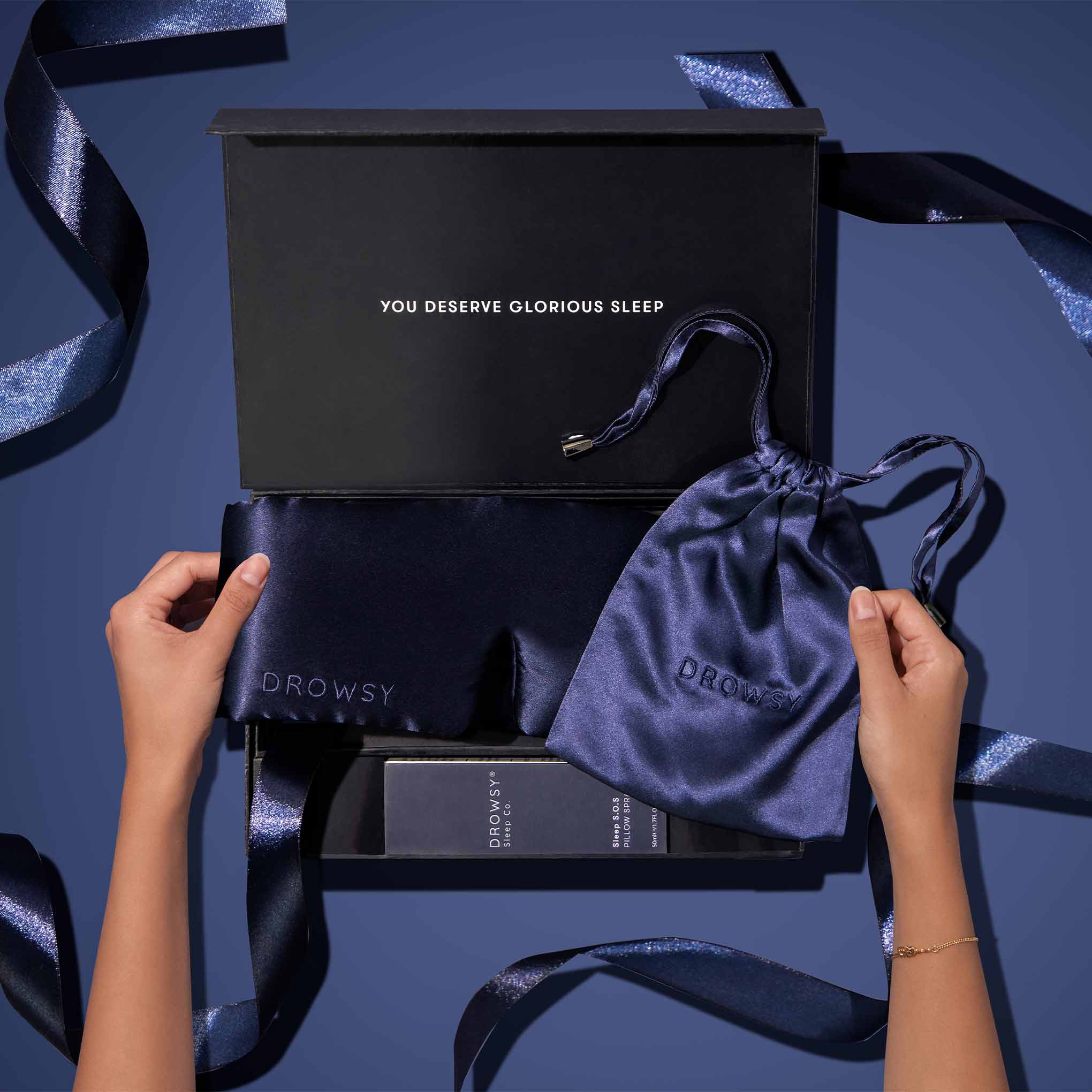 Drowsy Sleep Co. Midnight Blue gift box being unwrapped on a blue background